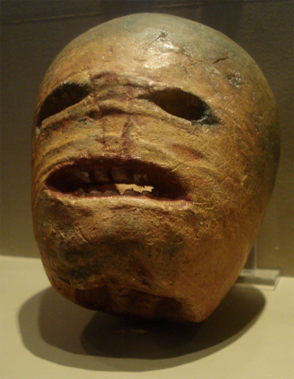 An old carved turnip lantern with hollow eyes and a wide, toothy grimacing mouth, displayed in a museum case