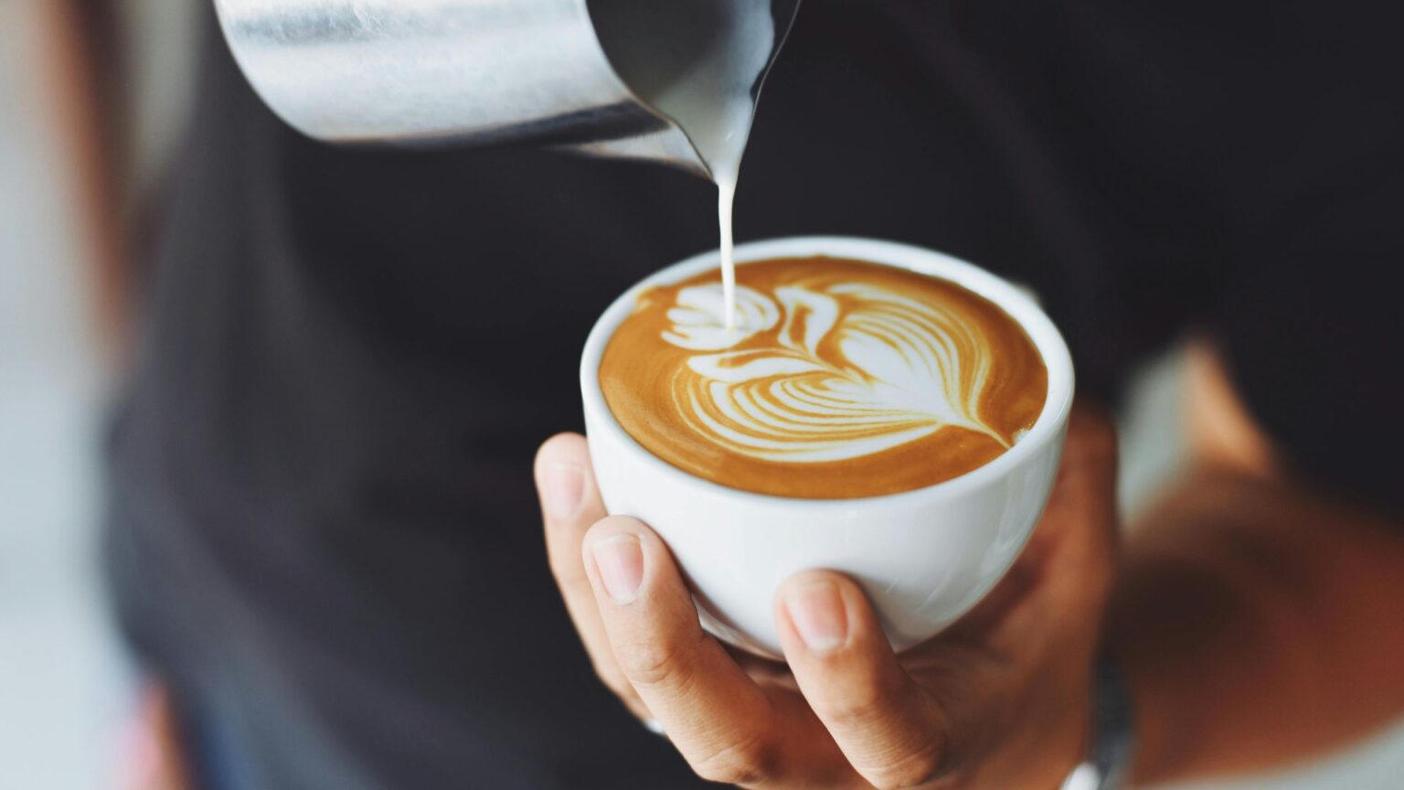 Barista pouring latte art in a white coffee mug