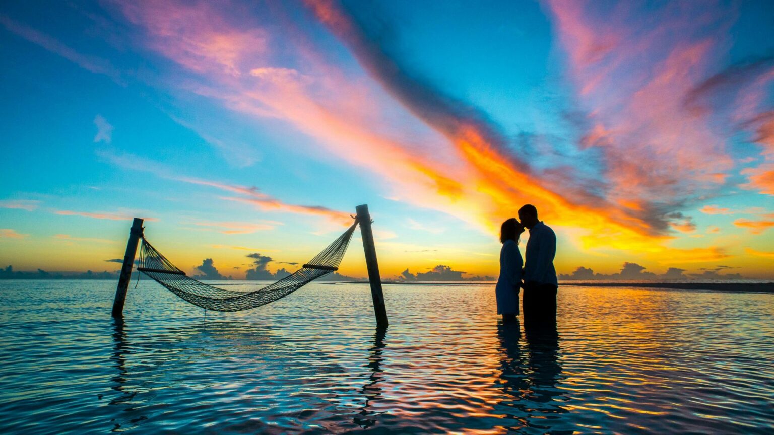 Sillouette of 2 people kissing in teh water in front of a colorful sunset