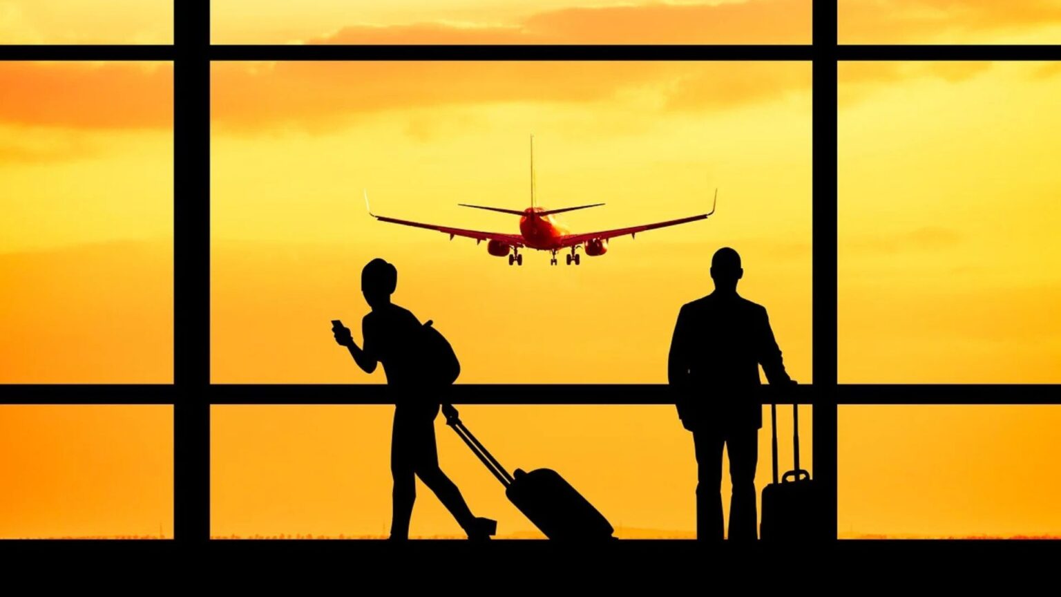 Two travelers looking out the airport window looking at a plane taking off