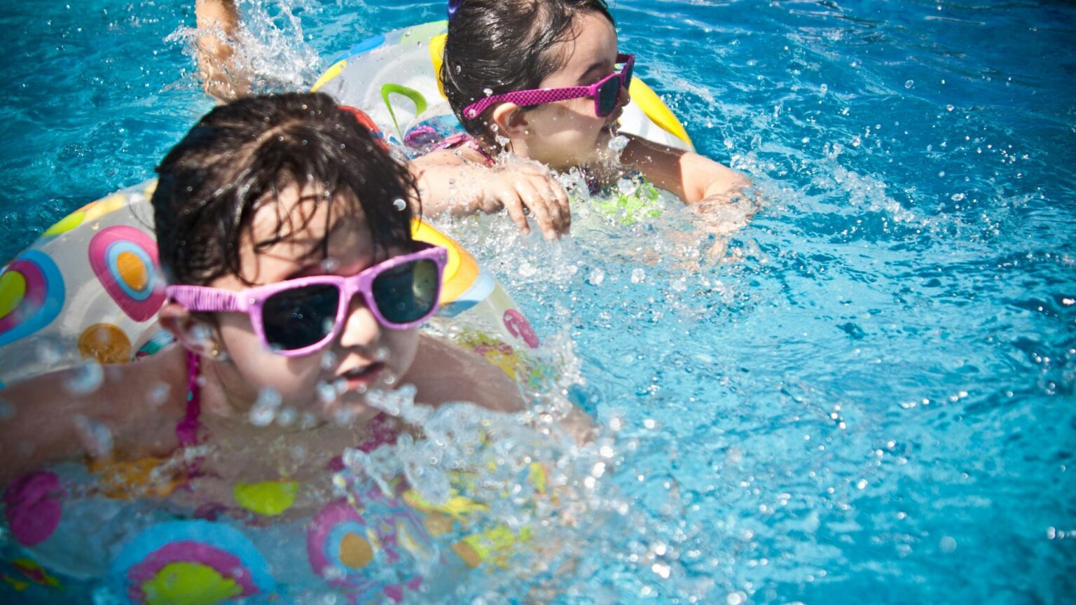 2 kids in sunglasses nad floaties in the pool