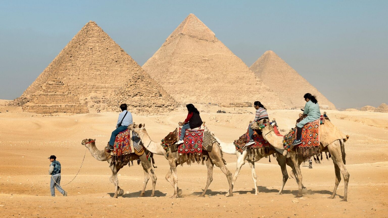 Four people on camals in front of the Great Pyramids